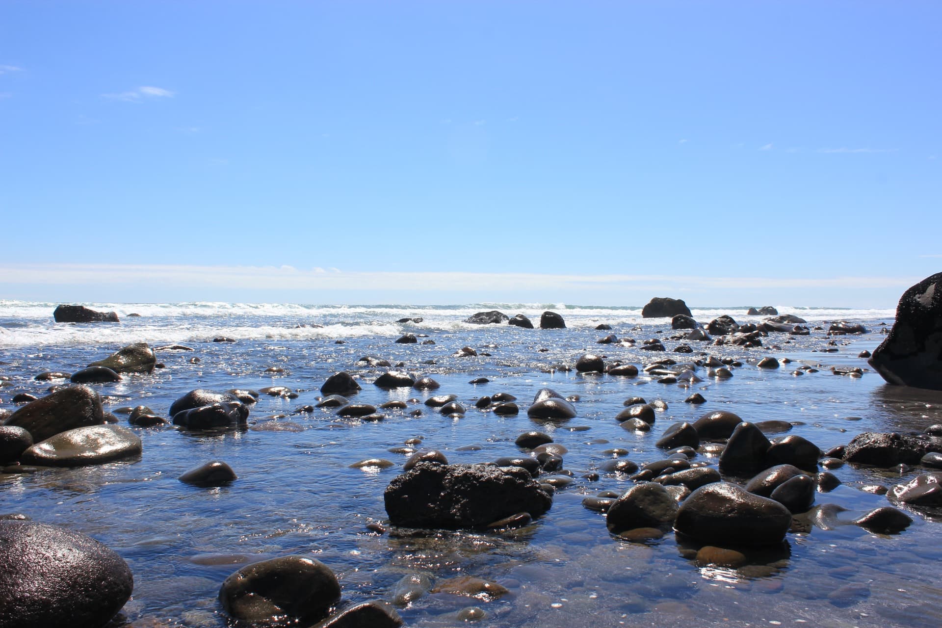 Wet black stones on a beach with waves in the background
